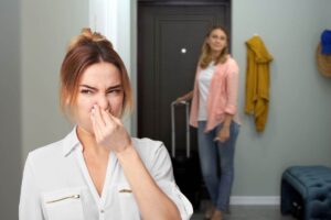 donna che rientra dalla porta con valigia e un'altra che sente cattivi odori