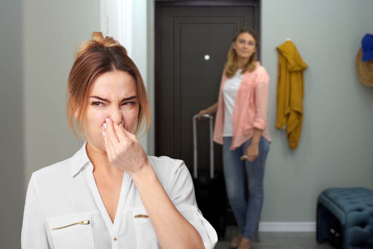 donna che rientra dalla porta con valigia e un'altra che sente cattivi odori