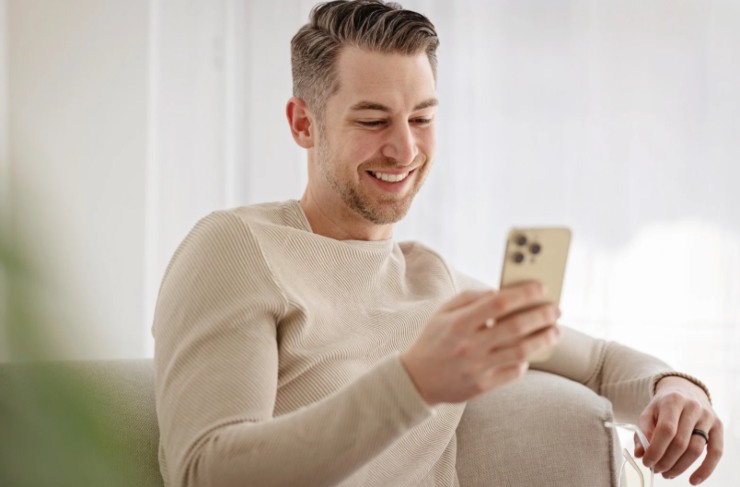 uomo seduto sul divano che sorride mentre guarda il cellulare